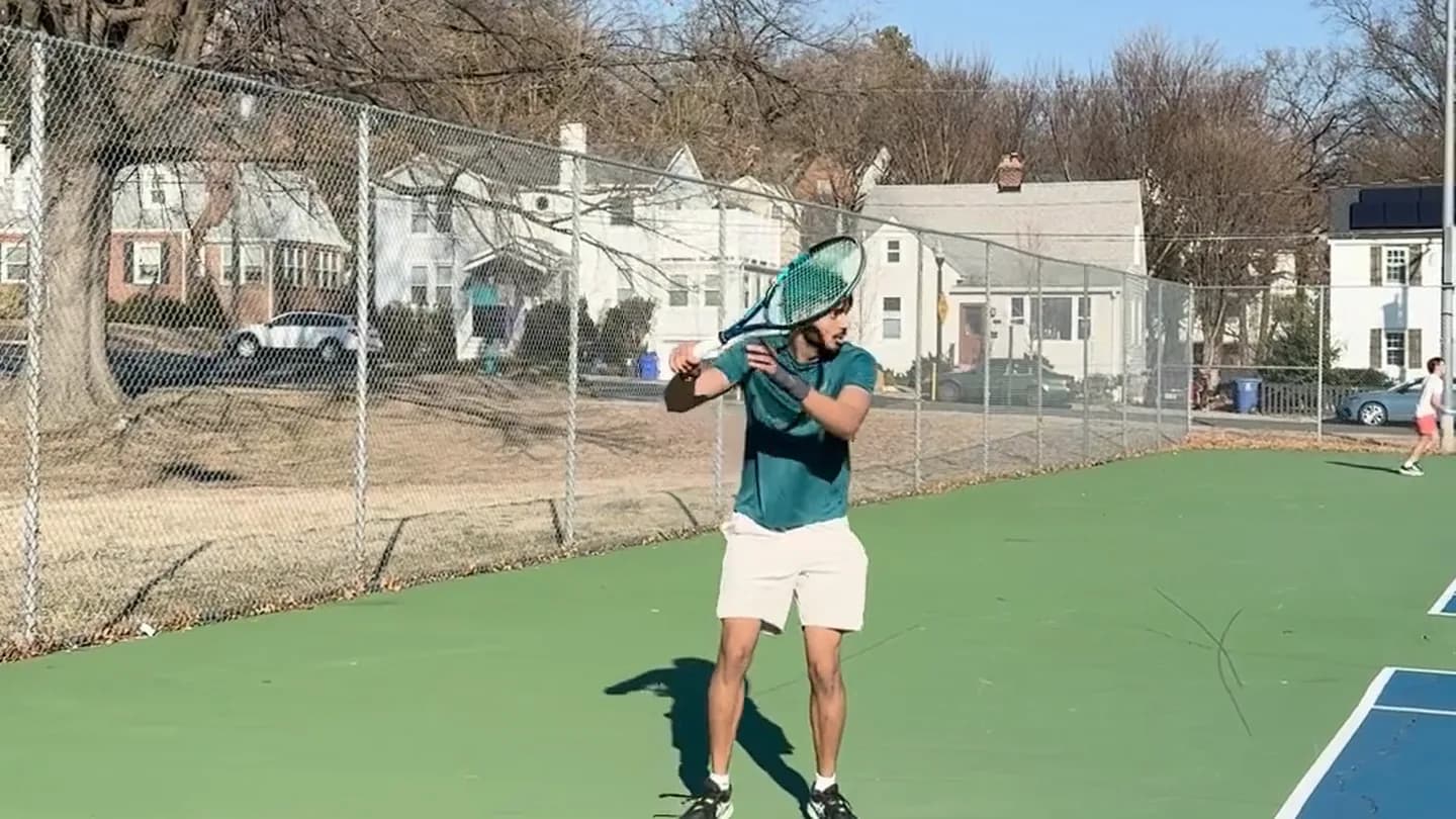 Coach Arun setting up for a two handed backhand during a practice session on an outdoor court