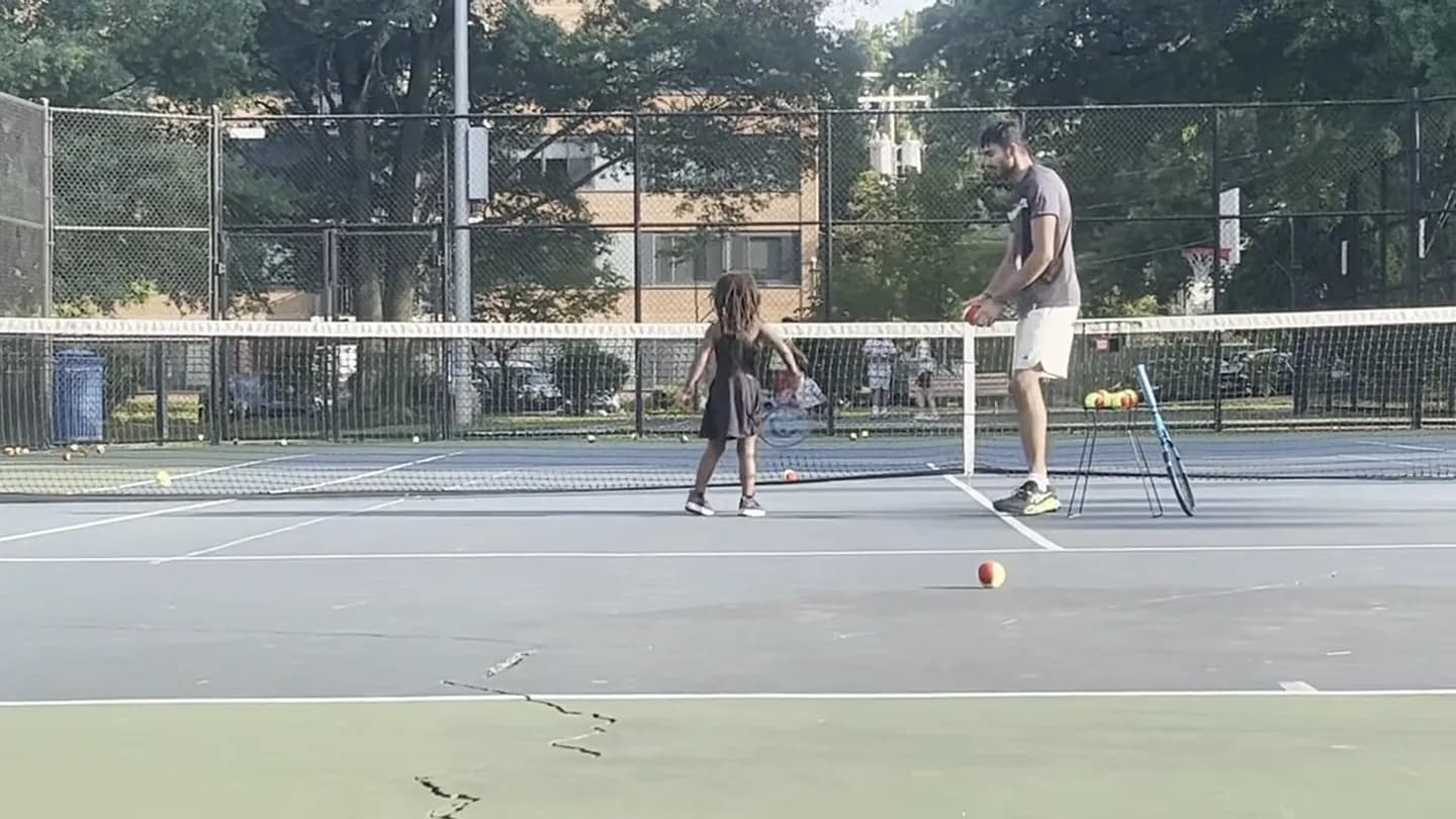 Coach Arun feeding balls to a young student beside a ball basket during a session on a Northern Virginia court